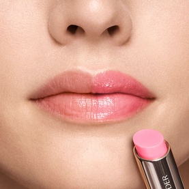 Model with Est&eacute;e Lauder Futurist HydraPlump Tinted Lip Balm in Petal Boost, shown on lips with balm stick displayed below