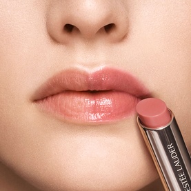 Model wearing Est&eacute;e Lauder Futurist HydraPlump Tinted Lip Balm in Rosewood Rescue, a sheer rosy nude, held beside glossy lips