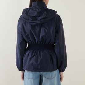 Model wearing Moncler Liriope Logo Raincoat in navy, shown from back, with elasticated waist and drawstring hood, styled with light-wash jeans.