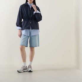 Model wearing Moncler Liriope Logo Raincoat in navy, styled with a blue stripe shirt, light blue shorts and white trainers.