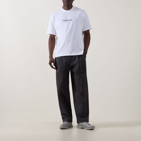 Model wearing Calvin Klein Standard Logo T-Shirt in Bright White with black wide-leg trousers and grey chunky trainers.