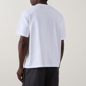 Model wearing Calvin Klein Standard Logo T-Shirt in Bright White, rear view, crew neck, dropped shoulders, paired with dark trousers.