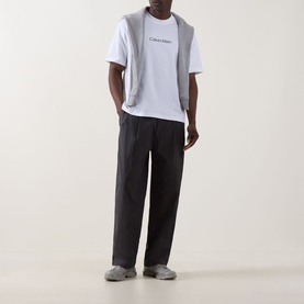 Model wearing Calvin Klein Standard Logo T-Shirt in Bright White with a grey gilet and black wide-leg trousers.