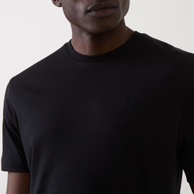 Model wearing Calvin Klein black crew neck T-shirt in 100% cotton, close-up showing chest detail with tonal logo embroidery.