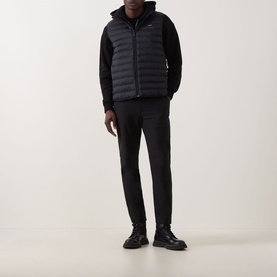 Model wearing Calvin Klein Logo Padded Gilet in black, styled with black hoodie, tapered trousers and chunky leather boots.