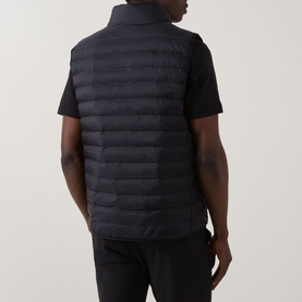 Model wearing Calvin Klein Logo Padded Gilet in black, rear view, showing quilted panels, standing collar and sleeveless silhouette over black