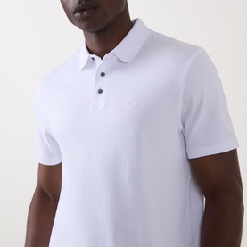Model wearing Calvin Klein Monogram Logo Polo Shirt in Bright White, featuring flat collar, button fastening and embroidered logo detail.