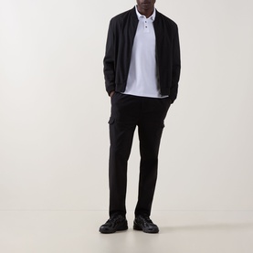 Model wearing Calvin Klein Monogram Logo Polo Shirt in Bright White with black bomber jacket, black trousers and black shoes.
