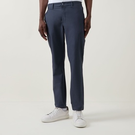 Model wearing Calvin Klein Tech Stretch Slim-Leg Trousers in Dark Sapphire, slim fit with clean hem, styled with white low-top trainers.