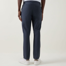 Model wearing Calvin Klein Tech Stretch Slim-Leg Trousers in Dark Sapphire, slim fit, rear welt pockets, styled with white trainers.