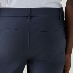 Model wearing Calvin Klein Tech Stretch Slim-Leg Trousers in Dark Sapphire, showing rear welt pockets and tonal stitching detail.