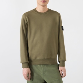 Model wearing Stone Island Verde Militare cotton sweatshirt with crew neck and signature arm badge patch, styled with matching cargo trousers.