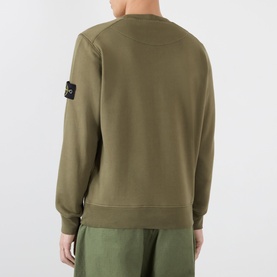 Model wearing Stone Island Verde Militare cotton sweatshirt, back view showing signature arm badge, paired with olive trousers.