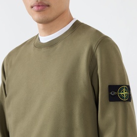 Model wearing Stone Island Verde Militare cotton sweatshirt with crew neck and signature compass badge on sleeve.