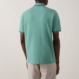 Model wearing Bugatti Double Tipped Logo Polo Shirt in mint, rear view showing tipped collar and cuffs, paired with light beige trousers.