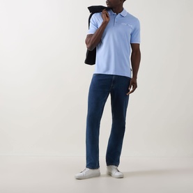 Model wearing Bugatti Contrast Tipped Polo Shirt in light blue with dark wash jeans and white trainers, jacket over shoulder.