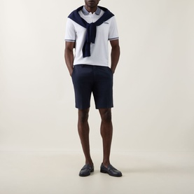 Model wearing Bugatti Contrast Collar Polo Shirt in white with navy collar and cuffs, styled with navy shorts and a navy sweater draped over