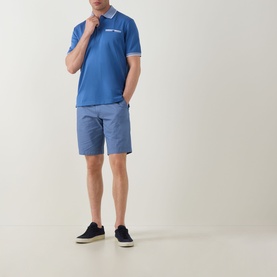 Model wearing Bugatti Tipped Logo Polo Shirt in dark blue with contrast tipping, styled with blue chino shorts and navy canvas shoes.