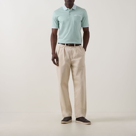 Model wearing Bugatti Patch Pocket Polo Shirt in mint with beige pleated trousers and dark brown loafers.
