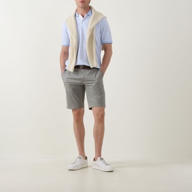 Model wearing Bugatti Stripe Logo Polo Shirt in light blue, styled with cream knit vest, grey shorts, and white trainers.