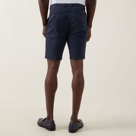 Model wearing Bugatti Twill Slim-Leg Shorts in navy, rear view, slim-leg cut above the knee with rear jetted pockets, styled with a white tee.