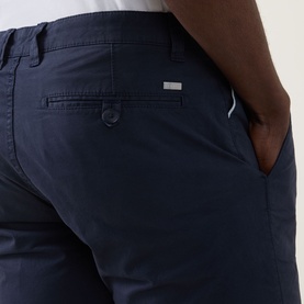 Model wearing Bugatti Twill Slim-Leg Shorts in navy, showing rear jetted pocket with button fastening and logo detail.