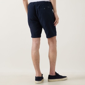 Model wearing Bugatti Lightweight Drawstring Shorts in navy, shown from behind, with navy canvas trainers.