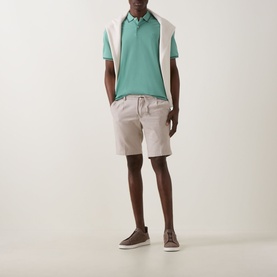 Model wearing Bugatti Lightweight Drawstring Shorts in stone with elasticated waist, styled with a green colourblock polo and brown trainers.