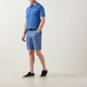 Model wearing Bugatti Summer Bermuda Shorts in light blue with belt loops, styled with a blue polo shirt and navy trainers.
