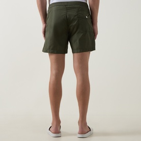 Model wearing Moncler green swim shorts, rear view, with white logo badge detail, styled with white slip-on shoes
