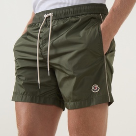 Model wearing Moncler green swim shorts with cream drawstring waist and logo badge, styled with a white tee