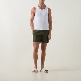 Model wearing Moncler green swim shorts with white vest top and white slider sandals.