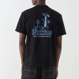 Model wearing Dickies Fairlawn Graphic T-Shirt in black, back view showing blue "All in a Day's Work" graphic print with tool characters.