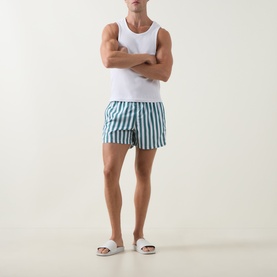 Model wearing Bjorn Borg blue and white vertical stripe swim shorts with white vest top and white slider sandals.