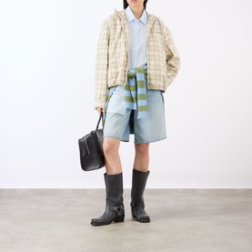 Model wearing Acne green/orange check cotton jacket, styled with blue shirt, light blue shorts, and black knee-high boots, carrying black tote bag