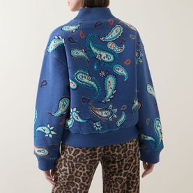 Model wearing Hayley Menzies Jimi Bandana Print Bomber Jacket in blue with all-over paisley print, styled with leopard-print trousers. Back view.