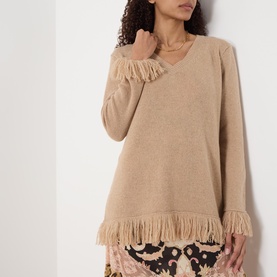 Model wearing Hayley Menzies Fringe Cashmere Sweater in camel, V-neckline, long sleeves, fringed hem and cuff trims, styled with printed skirt.