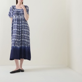 Model wearing Masai blue tie-dye midi dress with square neckline, short sleeves, and relaxed silhouette, styled with black flat shoes.