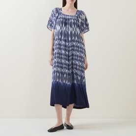 Model wearing Masai blue ikat-print midi dress with puff sleeves, smocked neckline and flared hem, styled with black flat shoes.