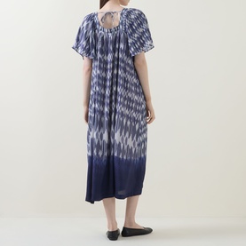 Model wearing Masai blue ikat-print midi dress with short puff sleeves, tie-dye hem, and keyhole back detail, styled with black flat shoes.