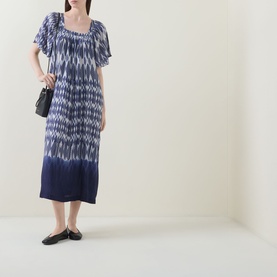 Model wearing Masai blue ikat-print midi dress with puff sleeves and smocked neckline, styled with black ballet flats and small black bag