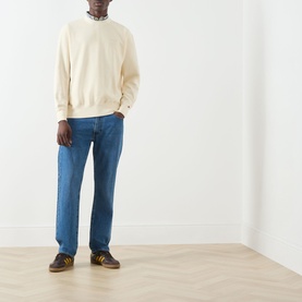 Model wearing Levis Garment Dye Rutabaga sweatshirt in cream, styled with blue straight-leg jeans and yellow trainers.