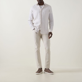 Model wearing Rodd & Gunn Gunn Straight-Leg Jeans in beige, styled with a white linen shirt and brown suede trainers.