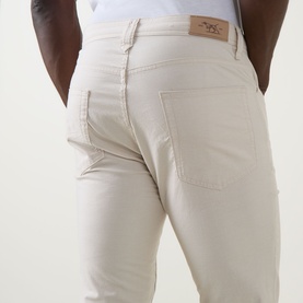 Model wearing Rodd & Gunn Gunn Straight-Leg Jeans in beige, showing rear five-pocket detail and logo patch at waistband.