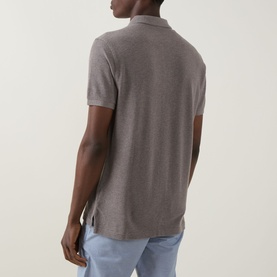 Model wearing Rodd & Gunn The Gunn Polo Shirt in Mocha, rear view showing split side seams and straight hemline, styled with light blue trousers.