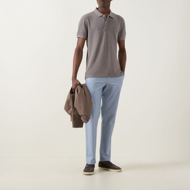 Model wearing Rodd & Gunn The Gunn Polo Shirt in Mocha with light blue trousers and dark loafers, carrying a tan jacket.