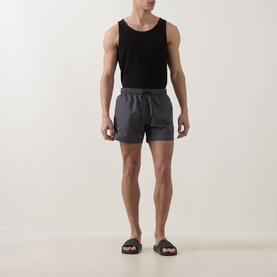 Model wearing Hugo black polyester swim shorts with elasticated waist, styled with a black vest and dark slider sandals.