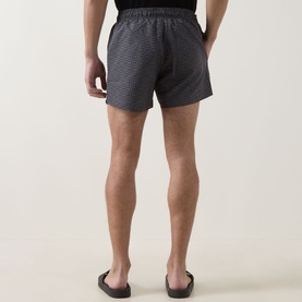 Model wearing Hugo black swim shorts with subtle textured pattern, shown from behind, styled with black slider sandals.