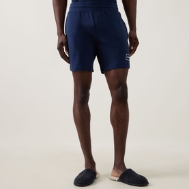 Model wearing Hugo Laze Logo Lounge Shorts in navy, mid-rise straight-leg cut with elasticated waist and logo badge, styled with dark slippers.