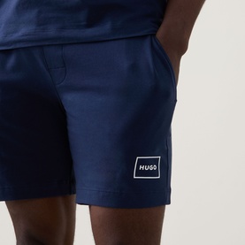 Model wearing Hugo Laze Logo Lounge Shorts in navy, straight-leg cut with elasticated waist and logo badge detail at hem.